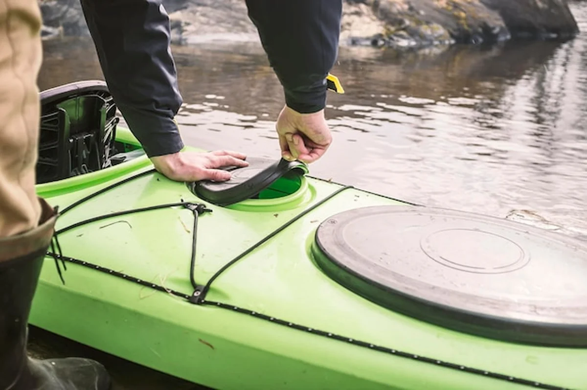 Mężczyzna otwiera hermetyczną pokrywę kajaka na brzegu jeziora, wiosenne popołudnie