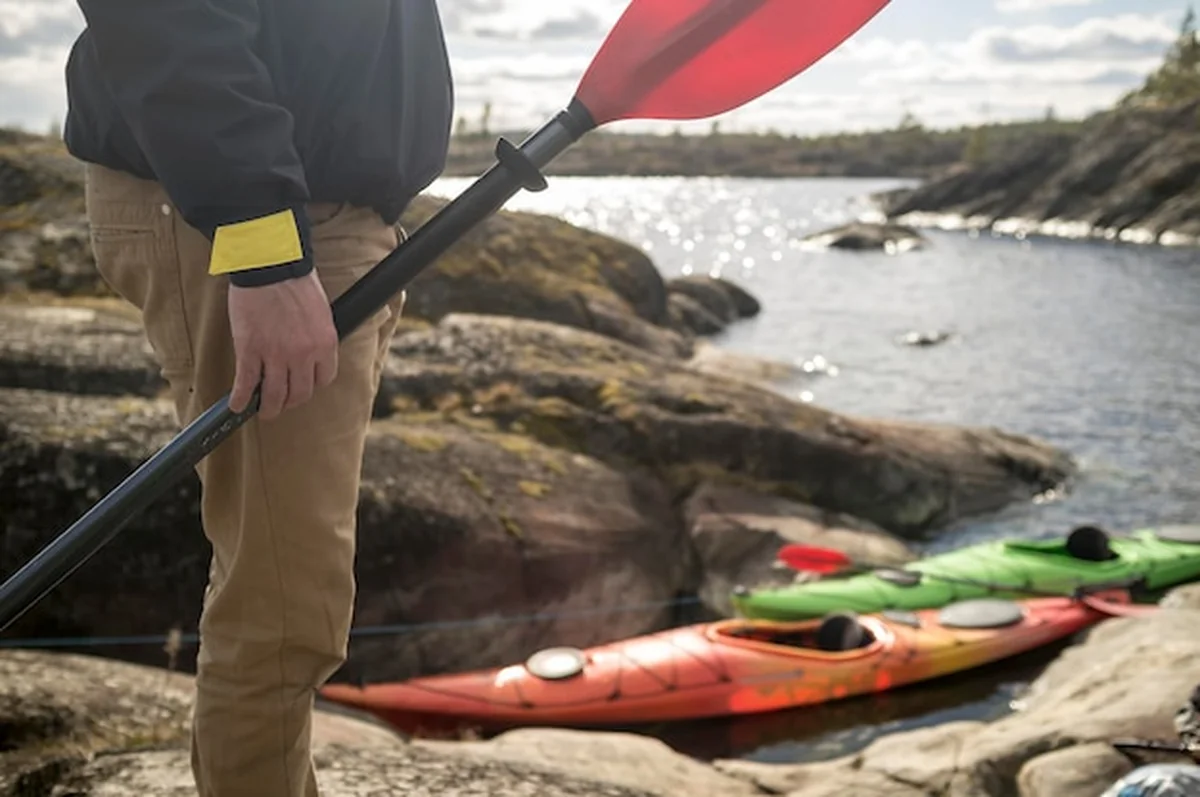 Mężczyzna z wiosłem na skalistym brzegu obok dwóch kajaków