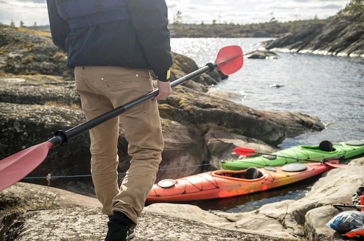 Mężczyzna z wiosłem na skalistym brzegu obok dwóch kajaków